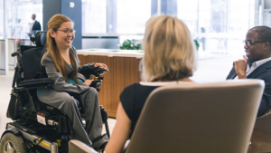 A person who is a wheelchair user seated with two other people in an office setting