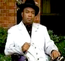 Timothy Elliot, a Black man who uses a wheelchair, wearing a white jacket and a black rimmed hat