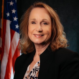 A professional headshot of Yvonne Wright against a dark blue background and the American flag.