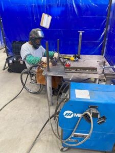 Larry Phillips, a black man who uses a wheelchair, working with welding tools while at work