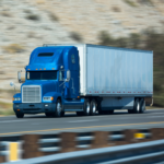 A blue and white semi truck driving down a hill-lined road