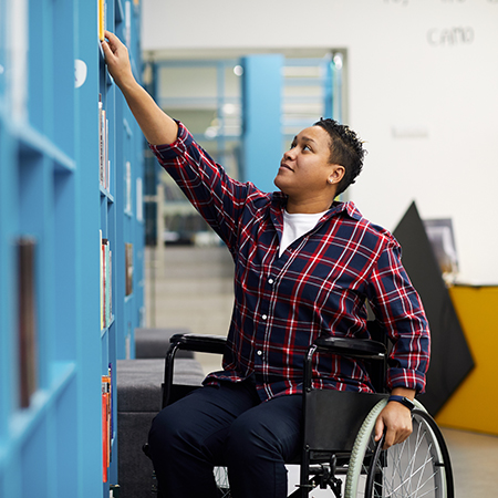 Portrait of a person who uses a wheelchair choosing books while studying in college library,